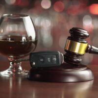 Drinking alcohol on driving ability The concept of a DUI. Law hammer, alcohol and car keys on wooden table, dark background