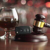 The concept of a DUI. Law hammer, alcohol and car keys on wooden table, dark background