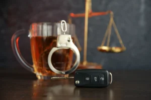 The concept of a DUI. Law hammer, alcohol and car keys on wooden table, dark background